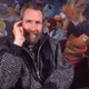 Jim Henson sits in a theater chair with Sesame Street's Ernie in front of a Muppets mural.